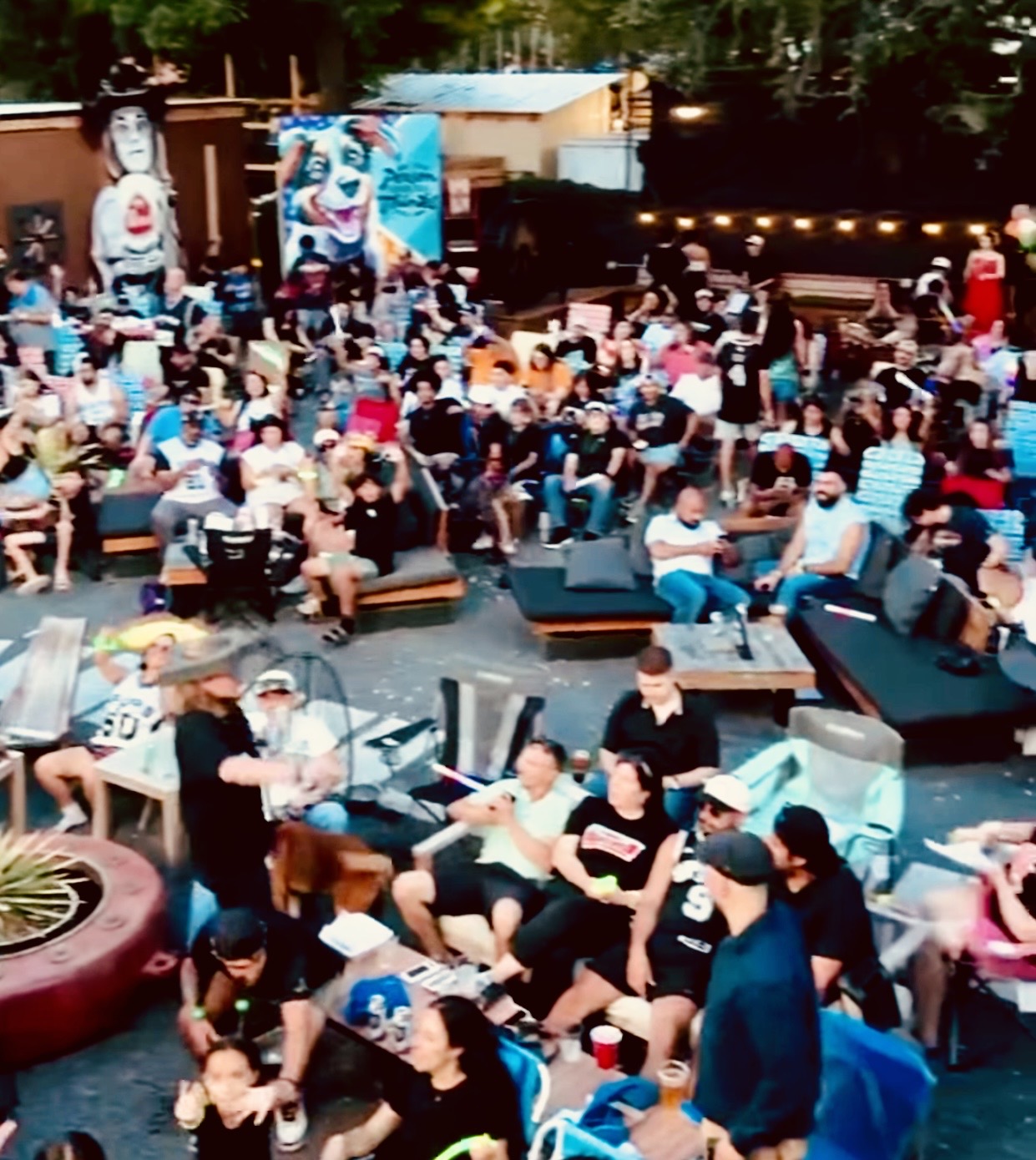 A crowd seated in the courtyard for a watch party under string lights