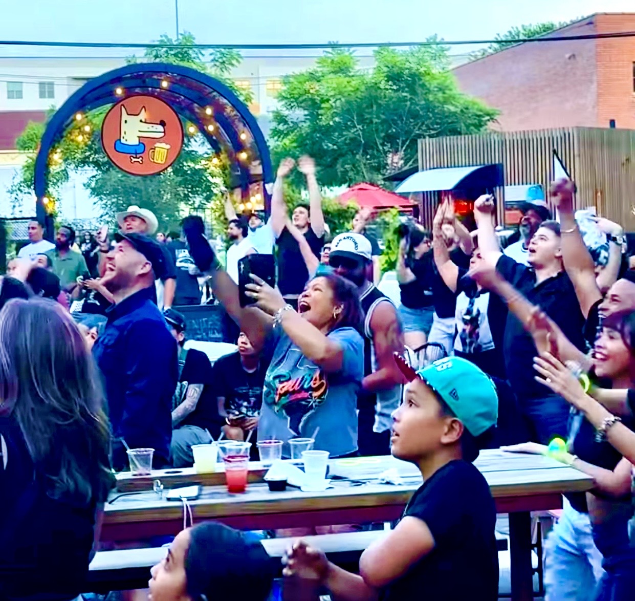 Guests cheering on the patio at dusk under the glowing Hops & Hounds sign