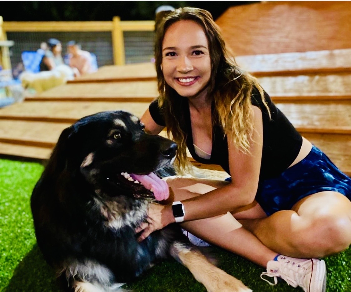A guest sitting on the turf with her dog at the Hops & Hounds dog park